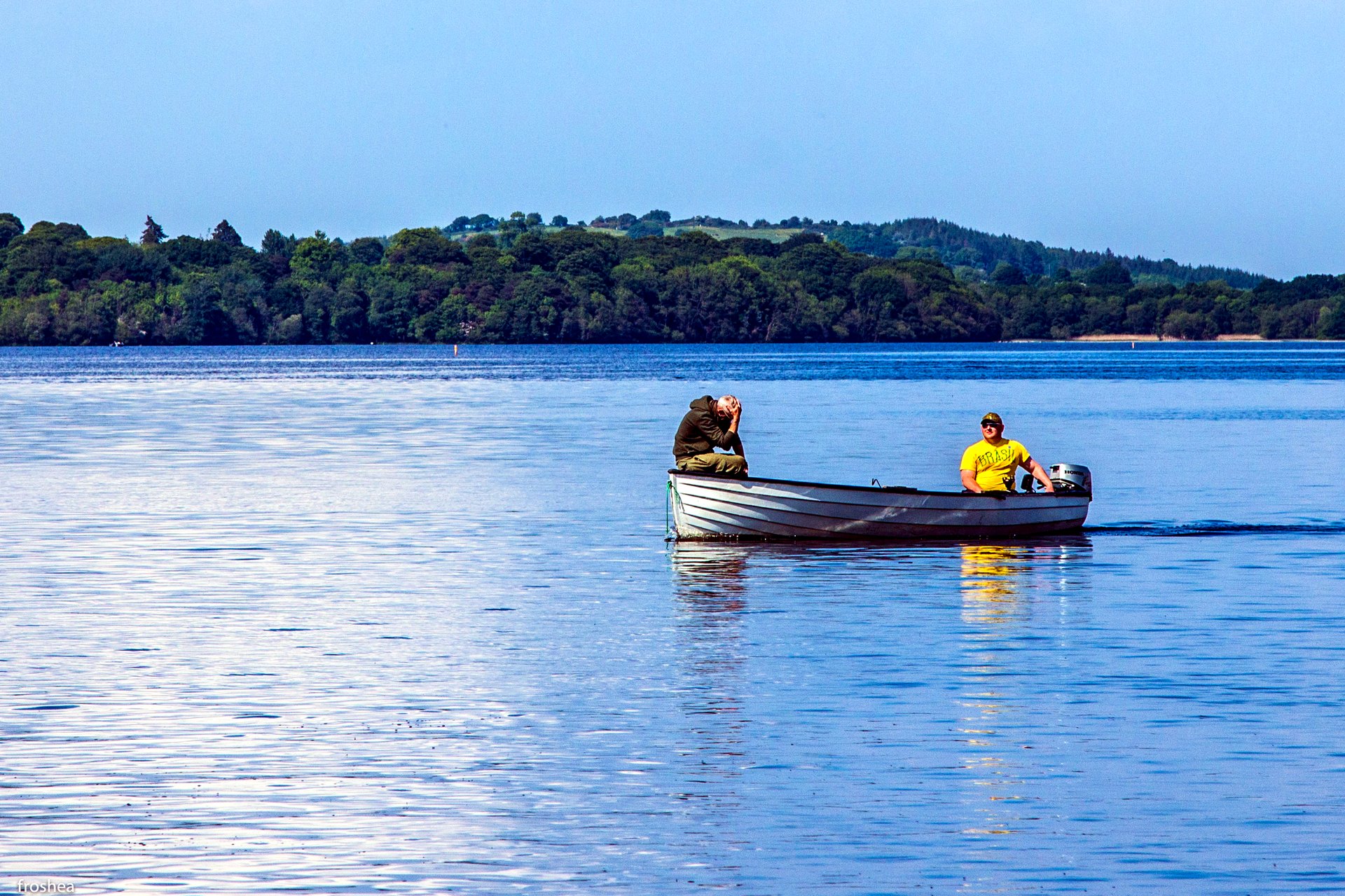 A small boat crossing the blue water of Lough Derg below wooded shores